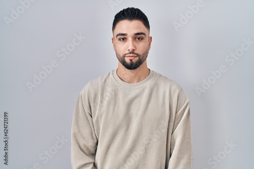 Young handsome man standing over isolated background relaxed with serious expression on face. simple and natural looking at the camera.