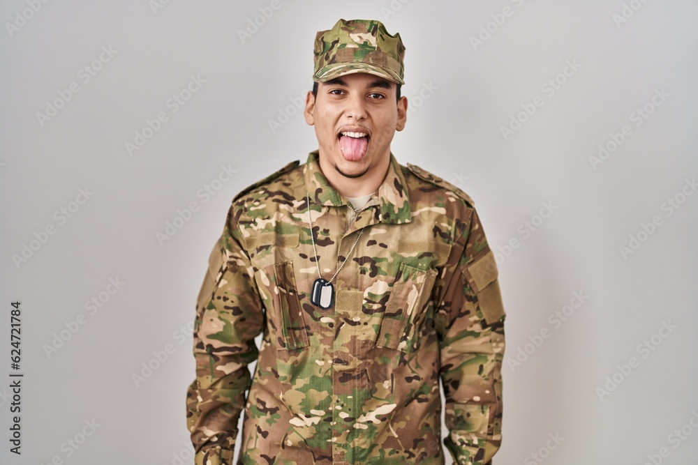 Young arab man wearing camouflage army uniform sticking tongue out happy with funny expression. emotion concept. Young arab man wearing camouflage army uniform sticking tongue out happy with funny expression. emotion concept.