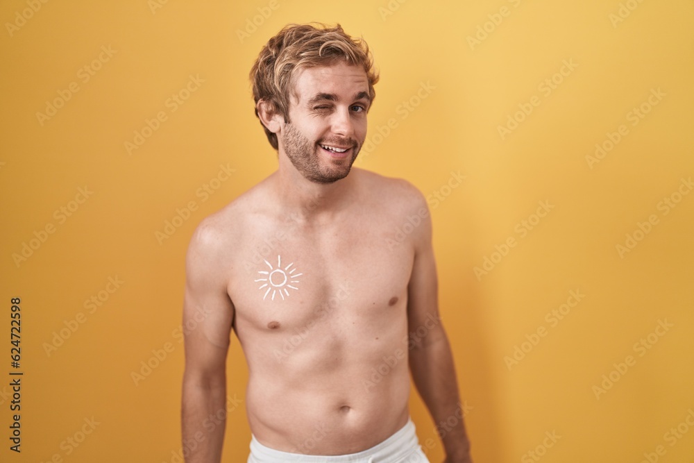 Fototapeta premium Caucasian man standing shirtless wearing sun screen winking looking at the camera with sexy expression, cheerful and happy face.