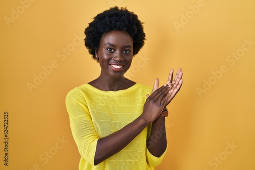 African young woman standing over yellow studio clapping and applauding happy and joyful, smiling proud hands together