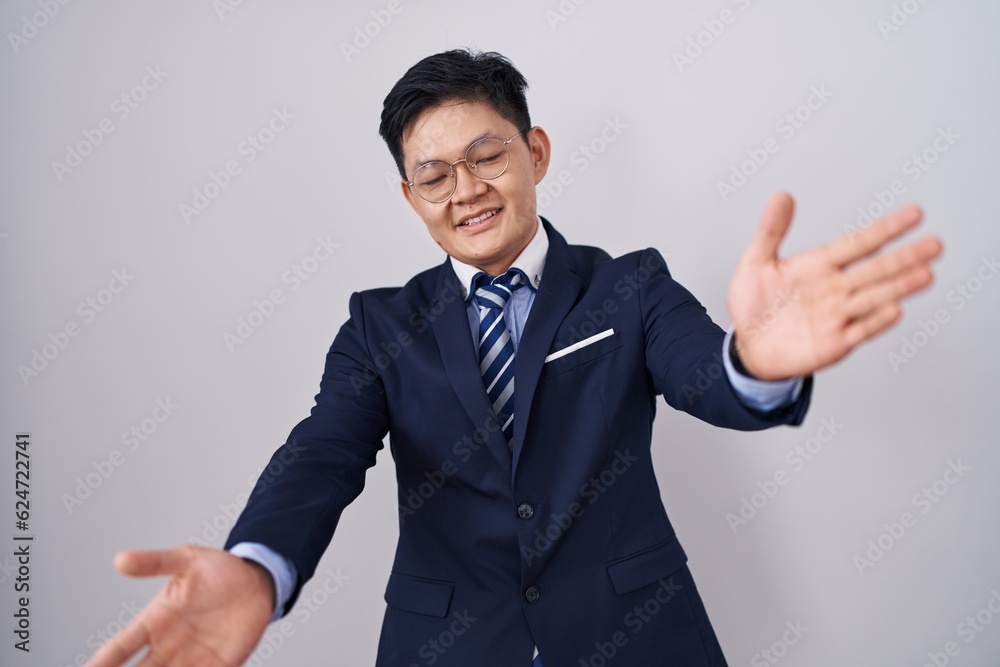 Young asian man wearing business suit and tie looking at the camera smiling with open arms for hug. cheerful expression embracing happiness. Young asian man wearing business suit and tie looking at the camera smiling with open arms for hug. cheerful expression embracing happiness.