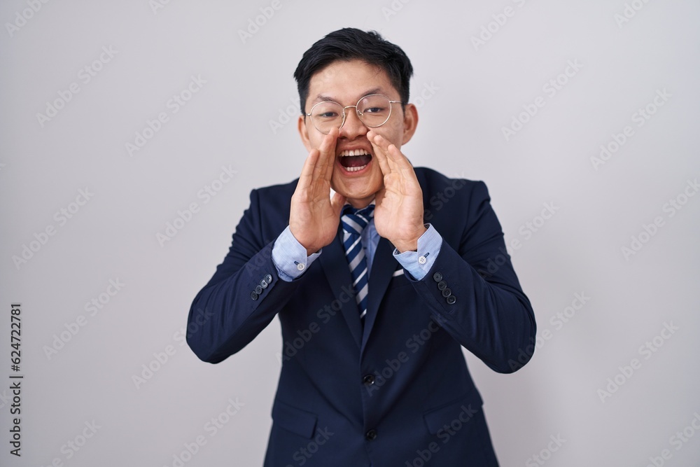 Young asian man wearing business suit and tie shouting angry out loud with hands over mouth Young asian man wearing business suit and tie shouting angry out loud with hands over mouth