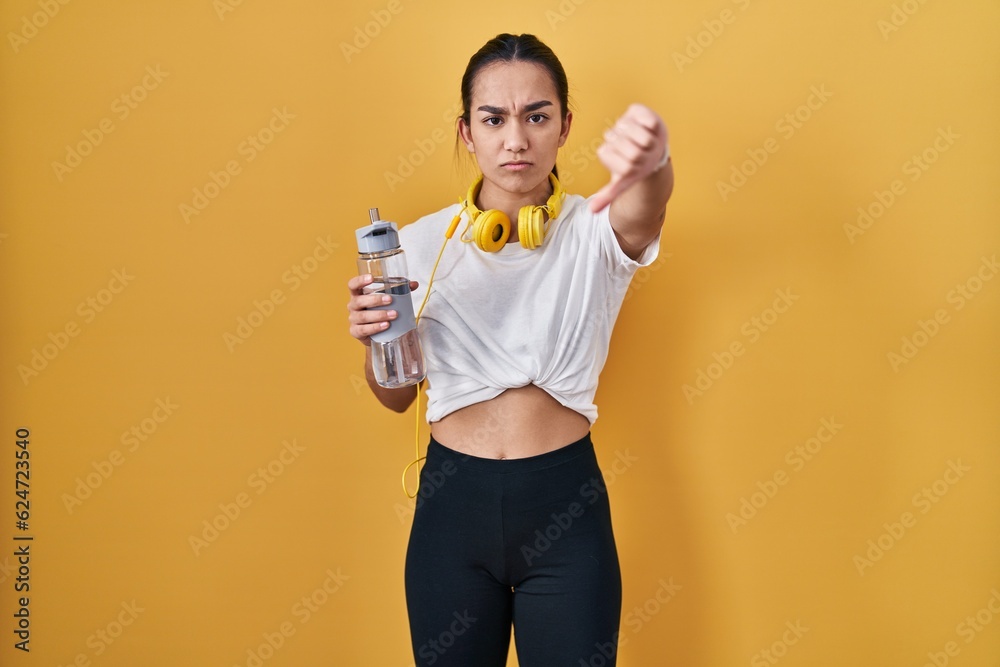 Young south asian woman wearing sportswear drinking water looking unhappy and angry showing rejection and negative with thumbs down gesture. bad expression. Young south asian woman wearing sportswear drinking water looking unhappy and angry showing rejection and negative with thumbs down gesture. bad expression.