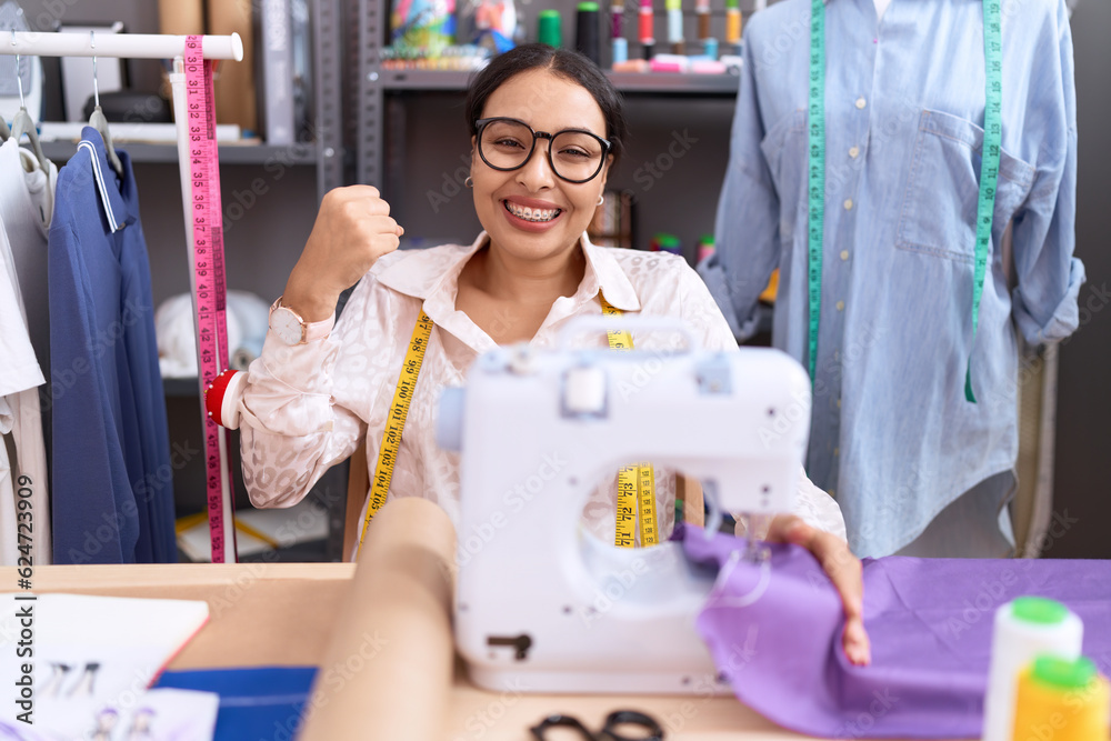 Young arab woman dressmaker designer working at atelier very happy and excited doing winner gesture with arms raised, smiling and screaming for success. celebration concept. Young arab woman dressmaker designer working at atelier very happy and excited doing winner gesture with arms raised, smiling and screaming for success. celebration concept.