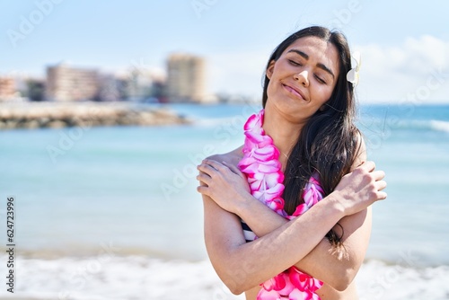 Young brunette woman wearing bikini at the beach hugging oneself happy and positive, smiling confident. self love and self care