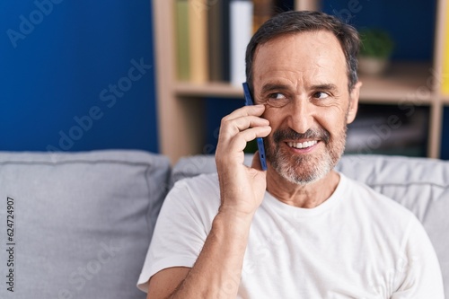 Middle age man talking on smartphone sitting on sofa at home