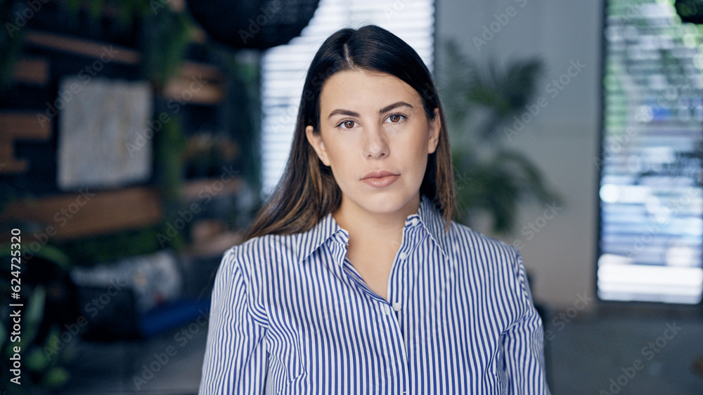 Young beautiful hispanic woman standing with serious face at the office