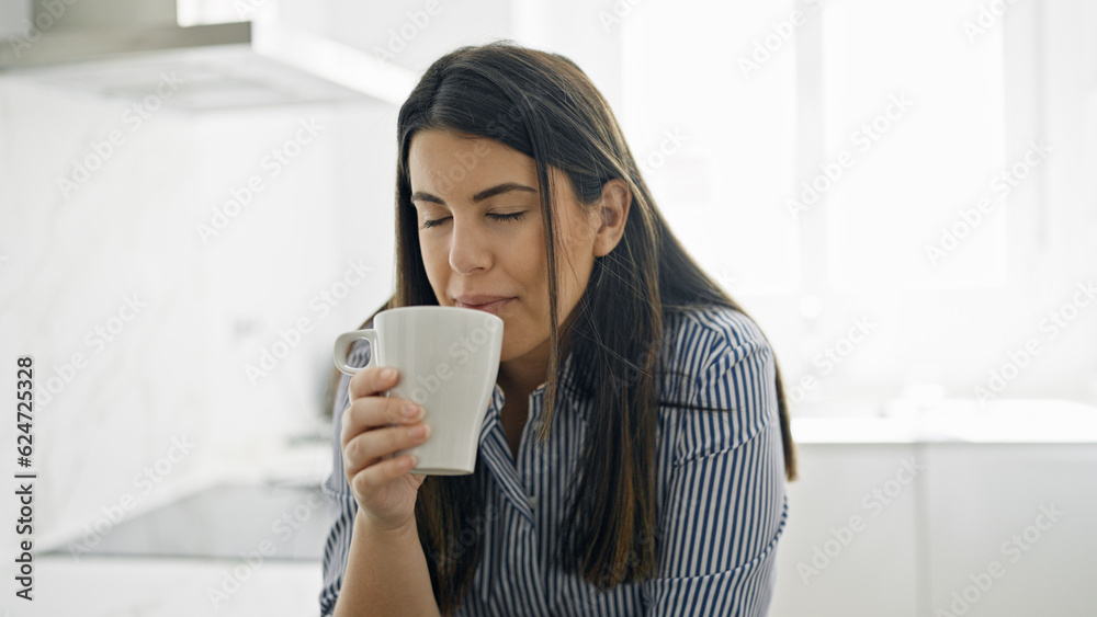 Young beautiful hispanic woman drinking a coffee leaning on the counter at the kitchen Young beautiful hispanic woman drinking a coffee leaning on the counter at the kitchen