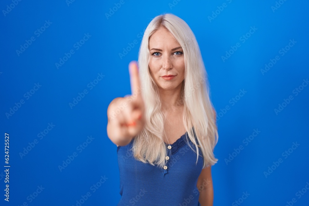 Fototapeta premium Caucasian woman standing over blue background pointing with finger up and angry expression, showing no gesture