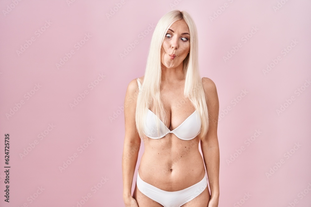 Fototapeta premium Caucasian woman wearing lingerie over pink background making fish face with lips, crazy and comical gesture. funny expression.