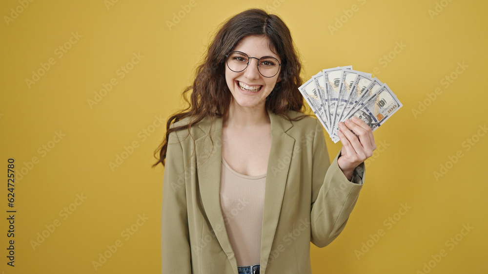 Young beautiful hispanic woman smiling confident holding dollars over isolated yellow background Young beautiful hispanic woman smiling confident holding dollars over isolated yellow background