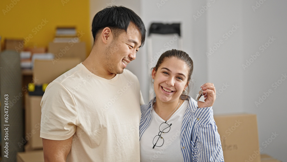 Fototapeta premium Man and woman couple hugging each other holding keys at new home