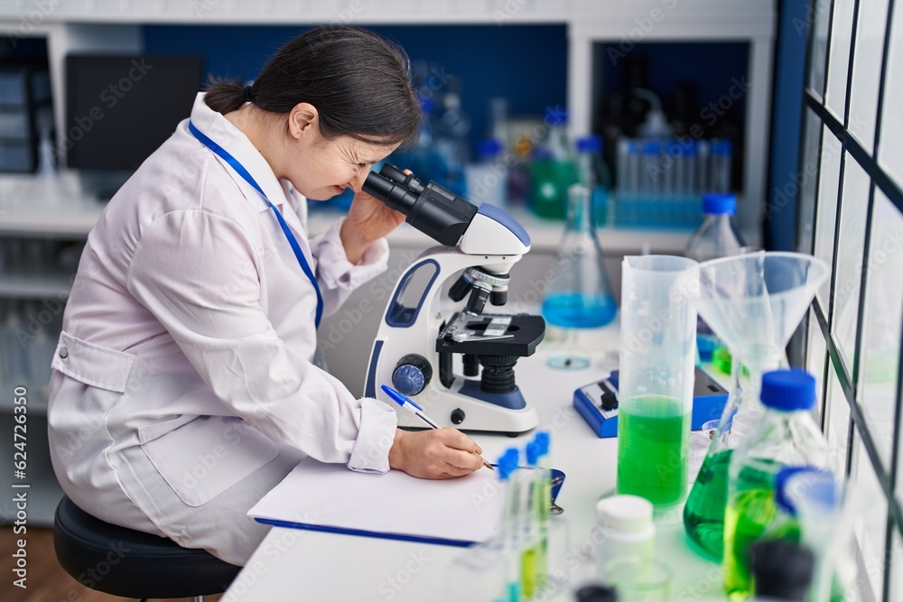 Young woman with down syndrome scientist using microscope write on document at laboratory Young woman with down syndrome scientist using microscope write on document at laboratory