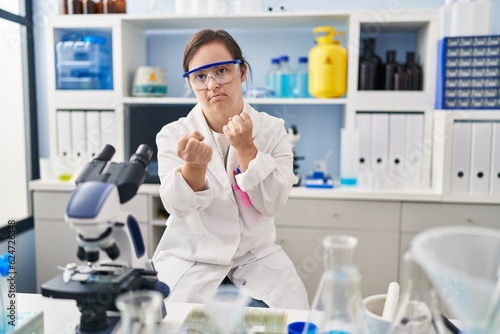 Hispanic girl with down syndrome working at scientist laboratory ready to fight with fist defense gesture  angry and upset face  afraid of problem