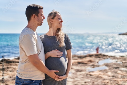 Man and woman couple standing together touching belly at seaside