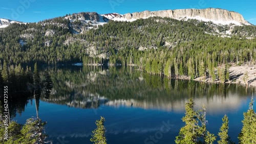 Aerial shot of a tranquil lake at dawn, reflecting the surrounded forest and mountains. In the Sierra Nevada Mountains near Mammoth Lakes California.