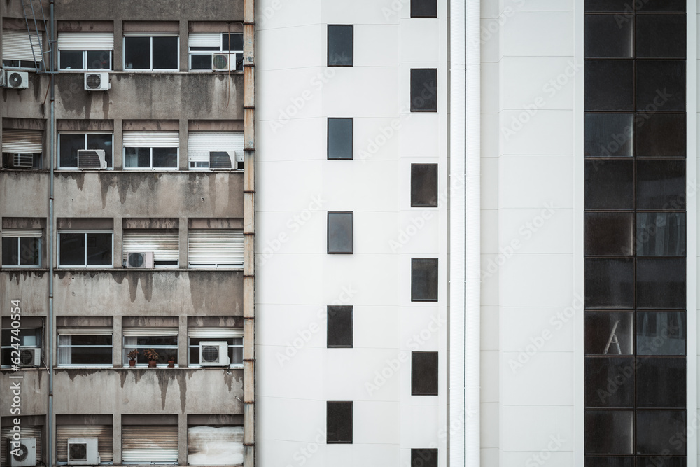 Contrasting facades, on the left, is a weathered apartment with multiple air conditioners, while on the right, a modern white dwelling with sleek rectangular windows forms a striking visual dichotomy Contrasting facades, on the left, is a weathered apartment with multiple air conditioners, while on the right, a modern white dwelling with sleek rectangular windows forms a striking visual dichotomy