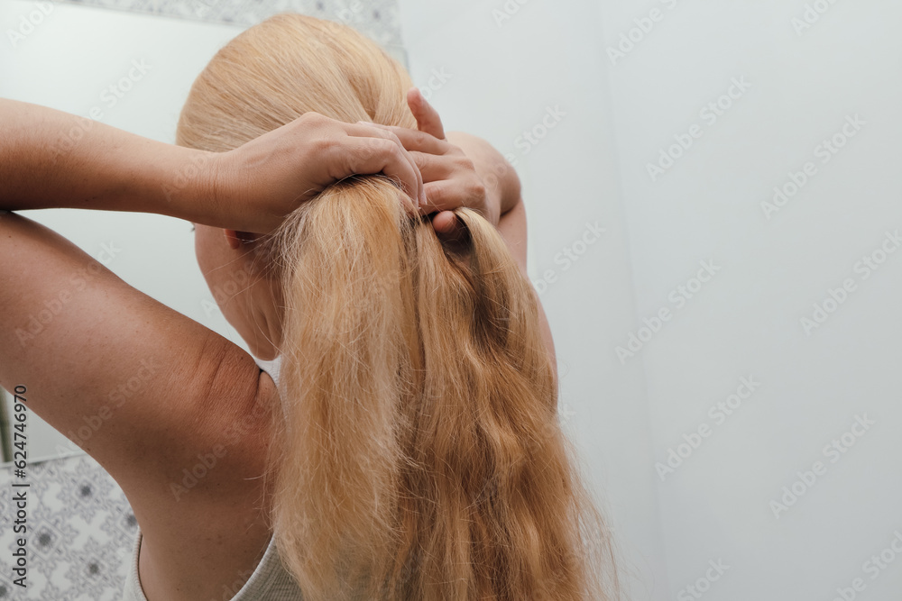 Naklejka premium Blonde woman braiding her hair, close up photo. Hair Braid. Rear view closeup. Woman tied her in braid at home