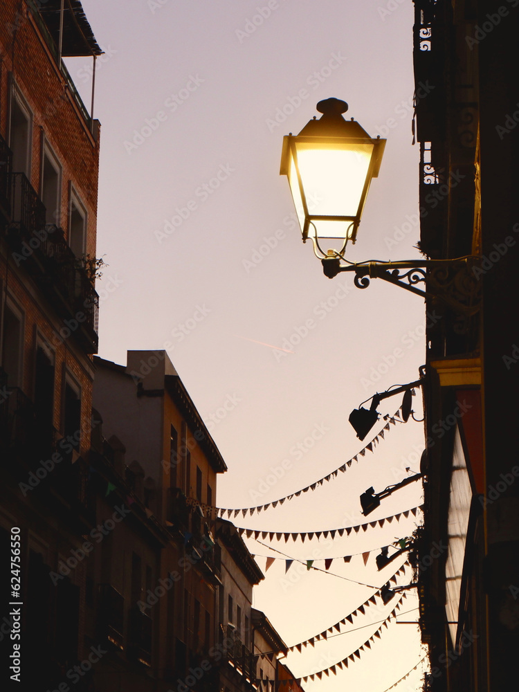 Lantern with warm light on facade of building downtown in Madrid, Spain. Twilight on narrow street, vintage illumination