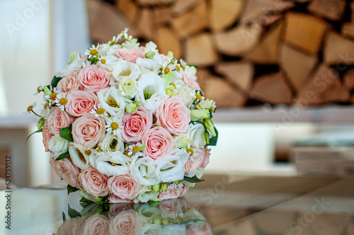 Gentle stylish wedding bouquet of roses and daisies on glass reflective surface in front of wooden logs, with copyspace