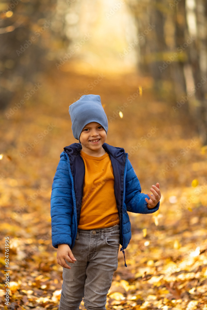 Happy little boy has fun in beautiful autumn park on warm sunny fall day. Child plays with golden maple leaves. Autumn foliage. Sun rays through the trees Happy little boy has fun in beautiful autumn park on warm sunny fall day. Child plays with golden maple leaves. Autumn foliage. Sun rays through the trees