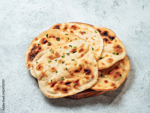 Fresh naan bread on plate over gray cement background. Several perfect naan flatbreads