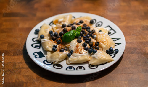 Traditional polish sweet cheese pierogi with blueberries, whipped cream, cinnamon and some basil decoration. Plate with sweet handmade dumpling dessert lunch or dinner on wooden table.