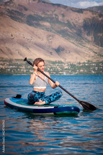 Girl rides a SUP board on the river on mountains background