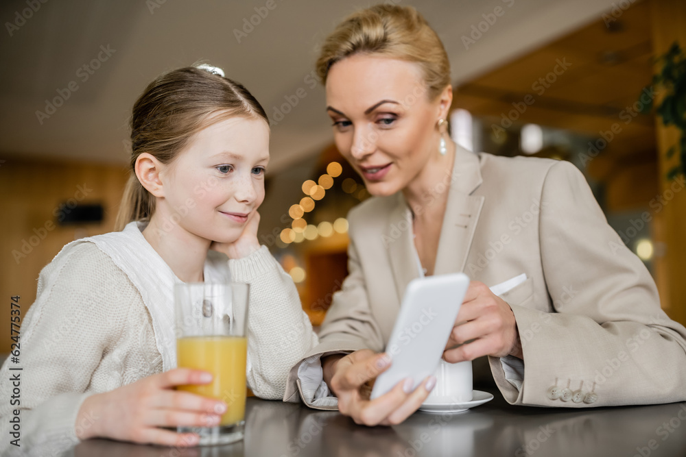 mother and daughter spending time together, blonde woman holding smartphone near daughter, working parent and child, modern parenting, family bonding, balanced lifestyle