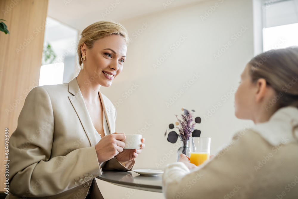 Obraz premium mother and daughter spending quality time together, cheerful blonde woman talking to preteen girl and holding cup of coffee, working parent and kid, modern parenting, family bonding, brunch