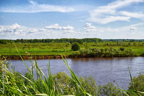 Beautiful landscape and nature with a view of the river and the sky with clouds through trees from high place. Green trees in foreground, water and greenery in background. Background and copy space