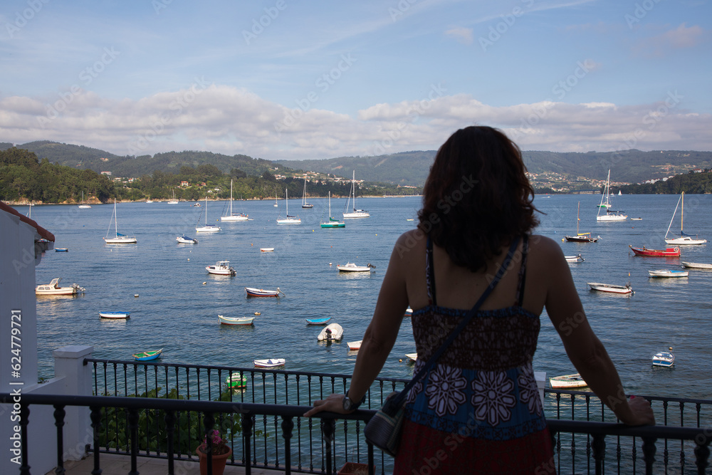 Paisaje marino del puerto de Redes, Galicia, España, con una turista mirando al mar.