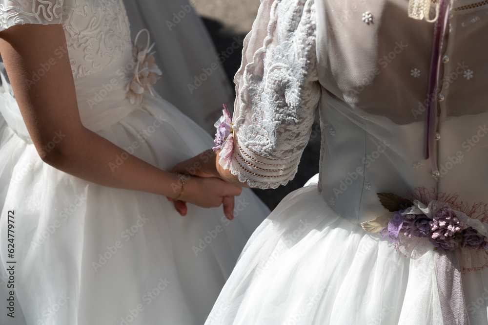 Obraz na płótnie Dos niñas de primera comunión con elegantes vestidos blancos se cogen de la mano. w salonie
