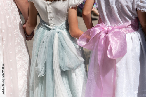 Print op canvas Niñas de primera comunión con elegantes vestidos blancos y lazos de colores caminan cogidas de la mano