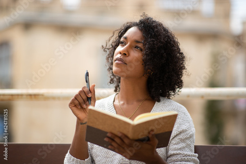 young african american woman thinking while writing in book