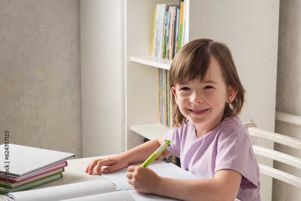 Girl sits at a table with books and a notebook and writes with her left hand. Left handed child. International Left Handers Awareness Day Girl sits at a table with books and a notebook and writes with her left hand. Left handed child. International Left Handers Awareness Day