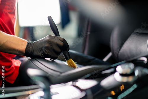 Car wash worker thoroughly cleaning the leather interior of a luxury car with a brush detailing close-up