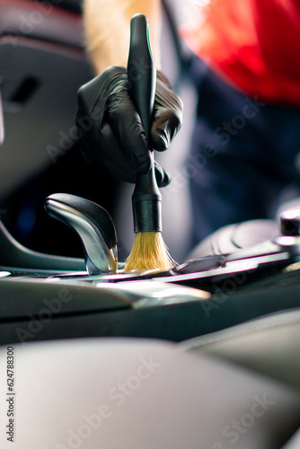 Car wash worker thoroughly cleaning the interior of a luxury car with a brush, gear box, close-up detailing