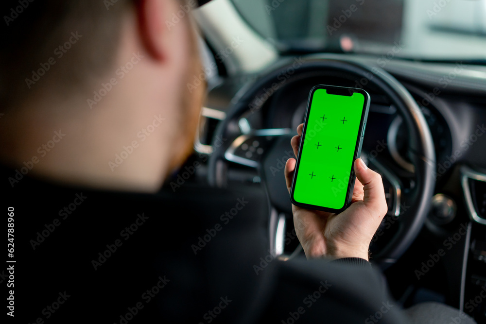 A man sits in a luxury car with a green screen phone in his hands