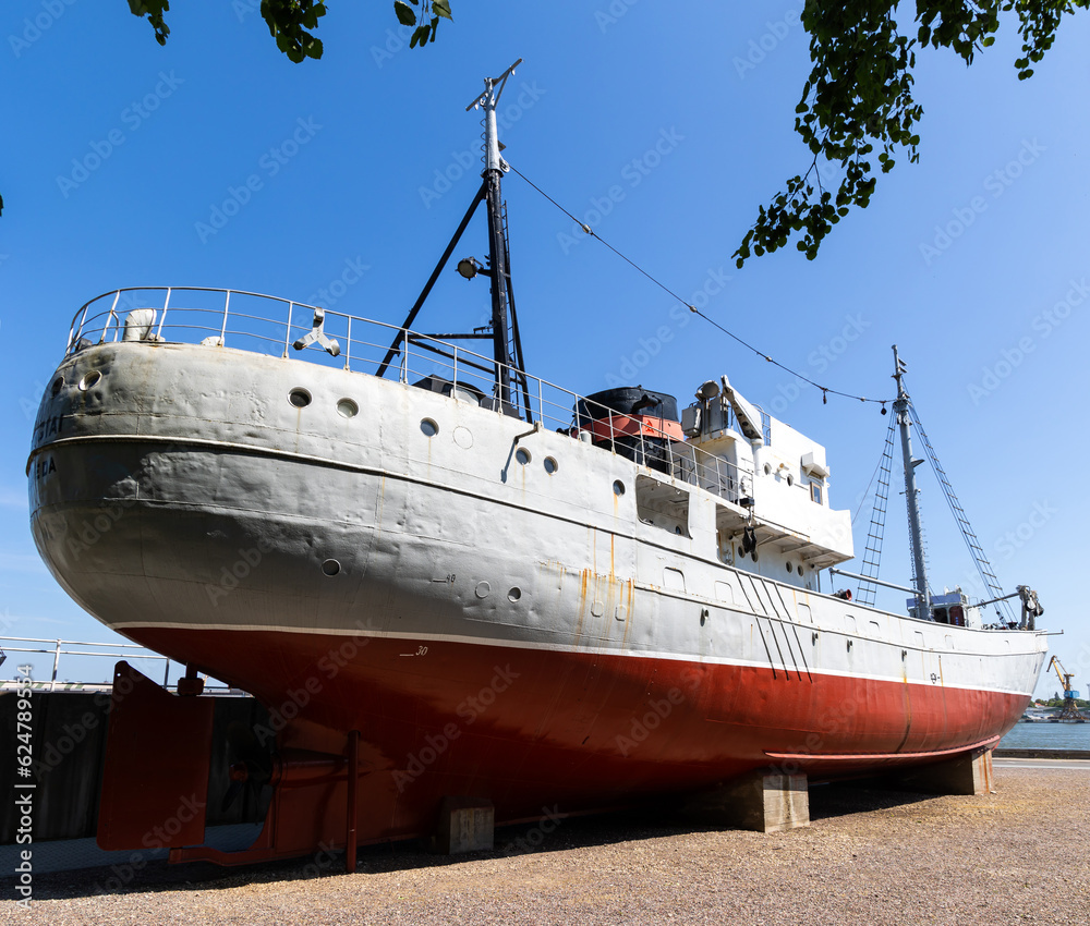Naklejka premium A historic fishing boat pulled out of the water and displayed on the museum's quay. Shot taken on a sunny day, the ship against the blue sky...