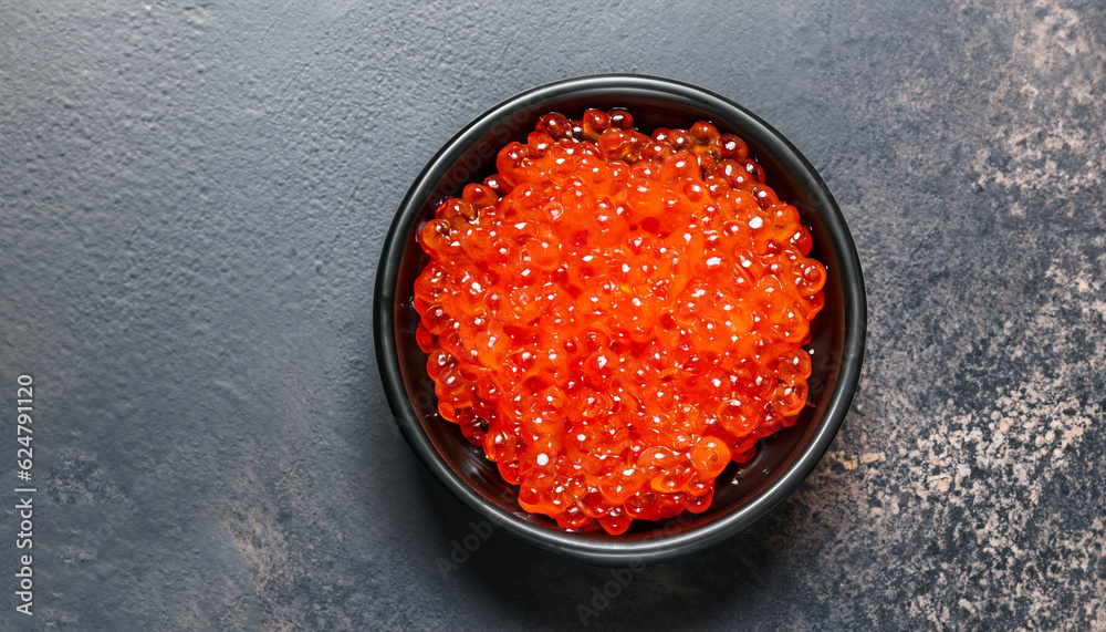 delicious red caviar in black bowl, top view, dark background