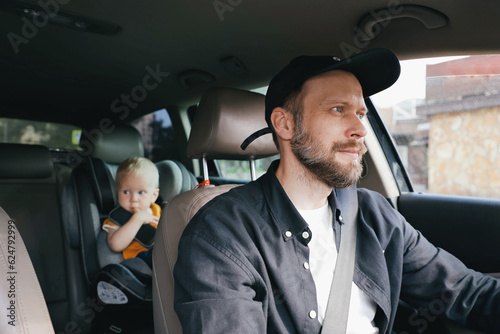 A man driving a car and a small child toddler in the back seat in a car seat