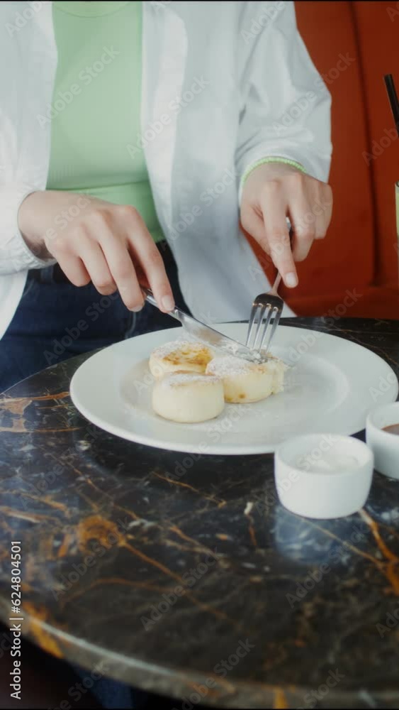 A young woman eats cheesecakes, cutting them with a knife, sitting at a table in a cafe A young woman eats cheesecakes, cutting them with a knife, sitting at a table in a cafe