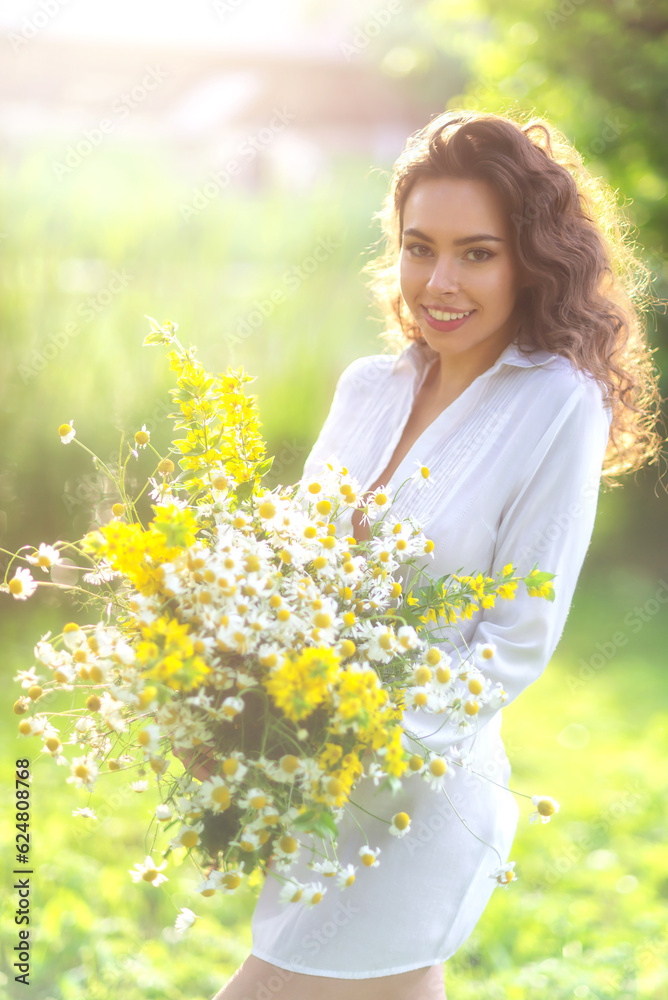 Portrait of a brunette with wild flowers on a background of nature in the summer at sunset. A girl in a white transparent shirt for the holiday of Ivan Kupala. Soft golden color Portrait of a brunette with wild flowers on a background of nature in the summer at sunset. A girl in a white transparent shirt for the holiday of Ivan Kupala. Soft golden color