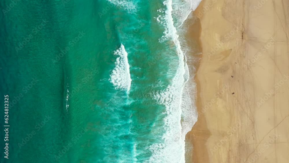 Tropical beach aerial view, Top view of waves break on tropical yellow sand beach. Sea waves seamless loop on the beautiful sand beach. Beautiful tropical beach aerial, bird's eye view of ocean waves.