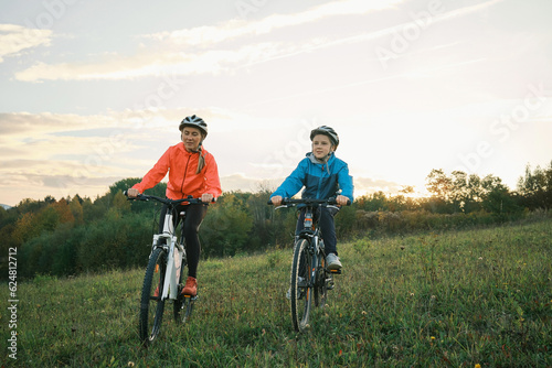 Mother and son ride a bike. Happy cute boy in helmet learn to riding a bike in park on green meadow in autumn day at sunset time. Family weekend.
