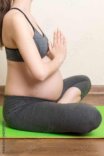 beautiful young pregnant woman sitting on mat in yoga pose at the home. Pregnancy Yoga and Fitness concept at coronavirus time