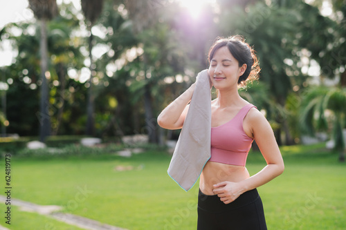 beauty of a healthy lifestyle as a 30s Asian woman in pink sportswear wipes her cheek after a morning run in nature. Experience the sense of accomplishment from achieving fitness goals.