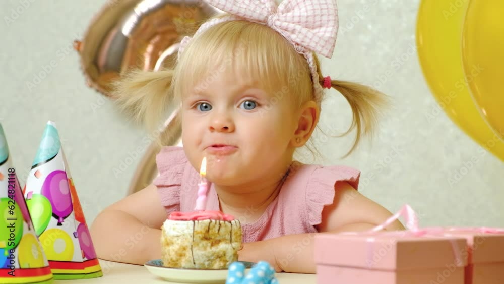 A two-year-old girl blows out a candle on a birthday cake, makes a wish A two-year-old girl blows out a candle on a birthday cake, makes a wish