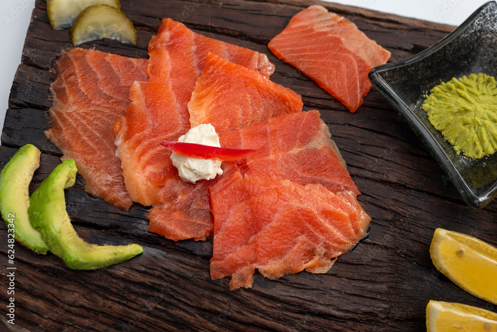 smoked salmon in fresh slices on a rustic wooden board with wasabi avocado, cheese, lemon pickles and soy sauce smoked salmon in fresh slices on a rustic wooden board with wasabi avocado, cheese, lemon pickles and soy sauce